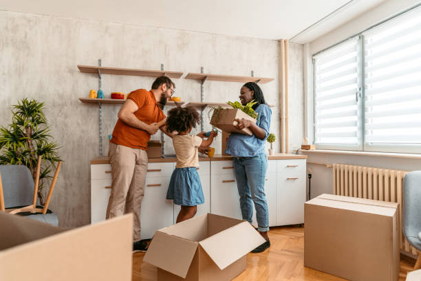 Pregnant black woman with her Caucasian husband and their child unpacking in their new apartment. Carrying boxes.