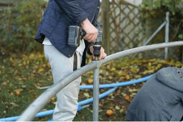 The image shows a person in dark clothing holding what appears to be a power tool while working on white metal railings or handrails, likely performing maintenance or installation work.